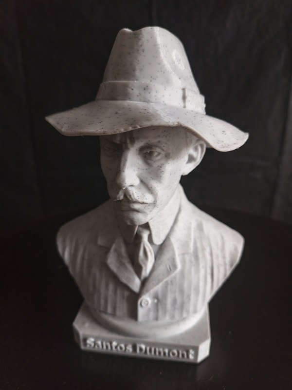 Busto de Santos Dumont impresso em 3D, com chapéu de aba larga, gravata e paletó, sobre base com a inscrição Santos Dumont